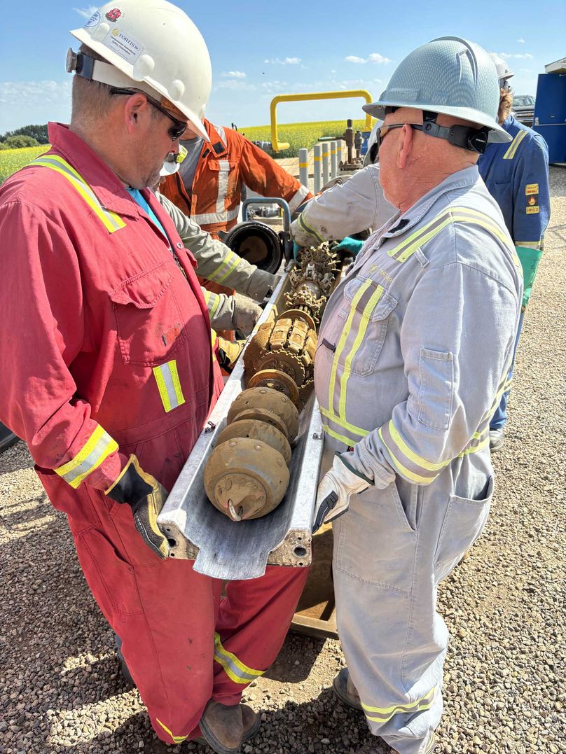 Two workers load a large robotic drill device into a pipe opening.