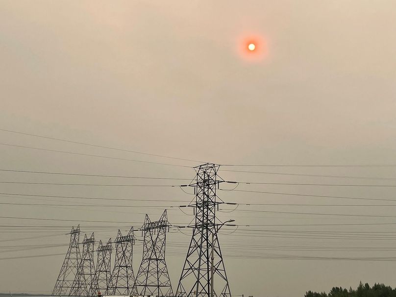The sun shines through a hazy, smoke-filled sky above power lines at the Kettle Generating Station.