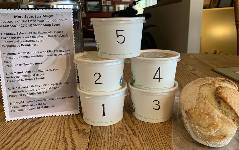 Cinq récipients à soupe et un mini pain au levain se trouvent à côté d’un menu décrivant toutes les soupes.