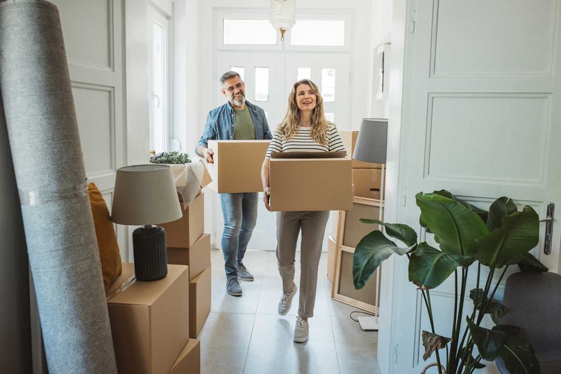 A couple carrying boxes in to a house