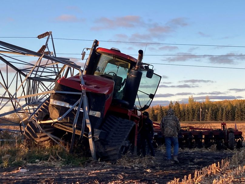 A tractor partially covered by a fallen steel transmission tower.