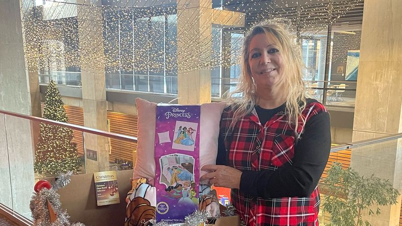 Female Manitoba Hydro employee stands beside Christmas Cheer Board donation box.