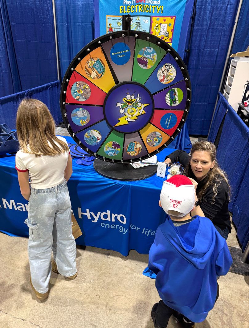 An adult crouches to talk to a kid in front of a colourful wheel of cartoons.