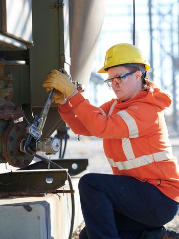 Woman in safety gear using a wrench to work on equipment in the outdoors.