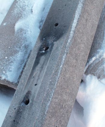 A concrete pole with blackened areas around some of the holes drilled into it.