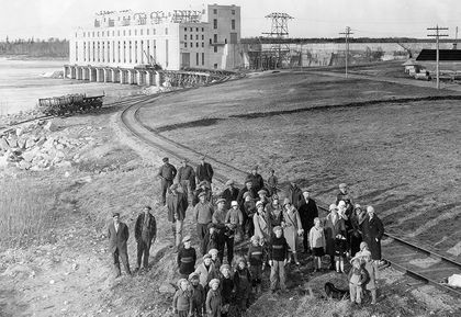 Employés, de leurs épouses et enfants à côté de la voie ferrée à l’extérieur de la centrale de Great Falls. La centrale est en arrière-plan.