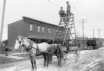 Deux hommes sur une grande échelle construite sur la plate-forme d’une charrette tirée par des chevaux.