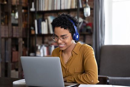 Young woman looking at a laptop wearing headphones.