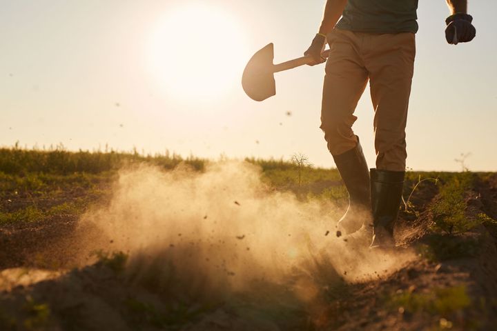 Un homme marche dans un champ poussiéreux avec une pelle.
