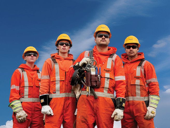 Four trainee power line technicians. One trainee has equipment over his shoulder.