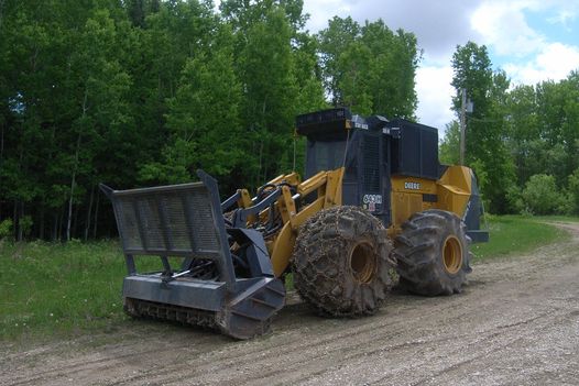 A large-wheeled yellow construction vehicle with a mulching attachment on the front used to clear vegetation along electrical infrastructure.